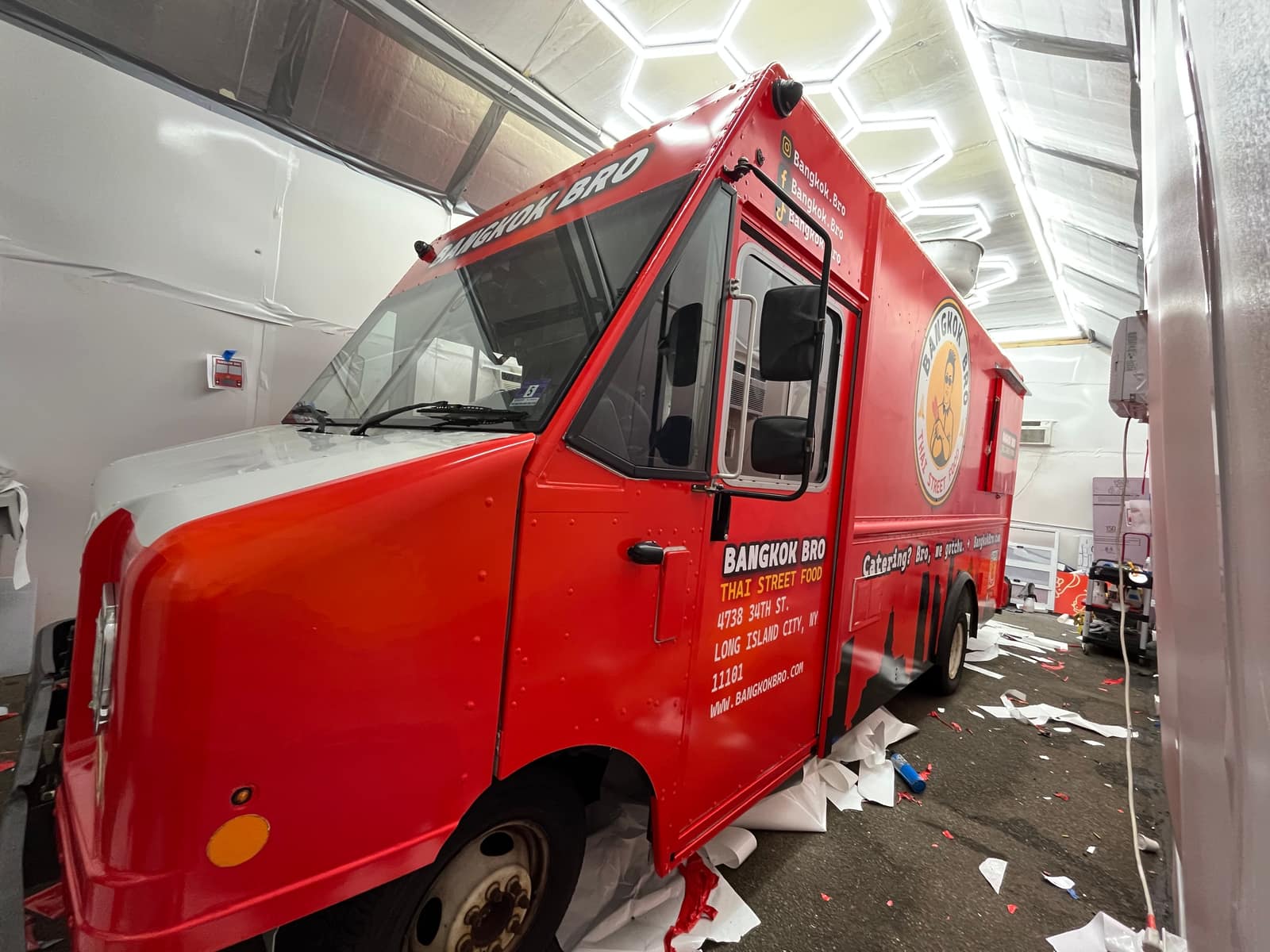 Red Bangkok Bro food truck being wrapped in the shop, side view with the serving window area and roof lettering