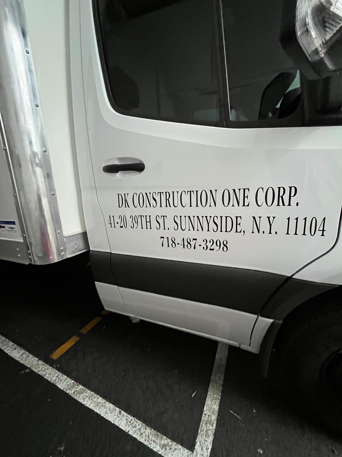 White Sprinter door with cut vinyl lettering for DK Construction One Corp, showing the Sunnyside address and phone number