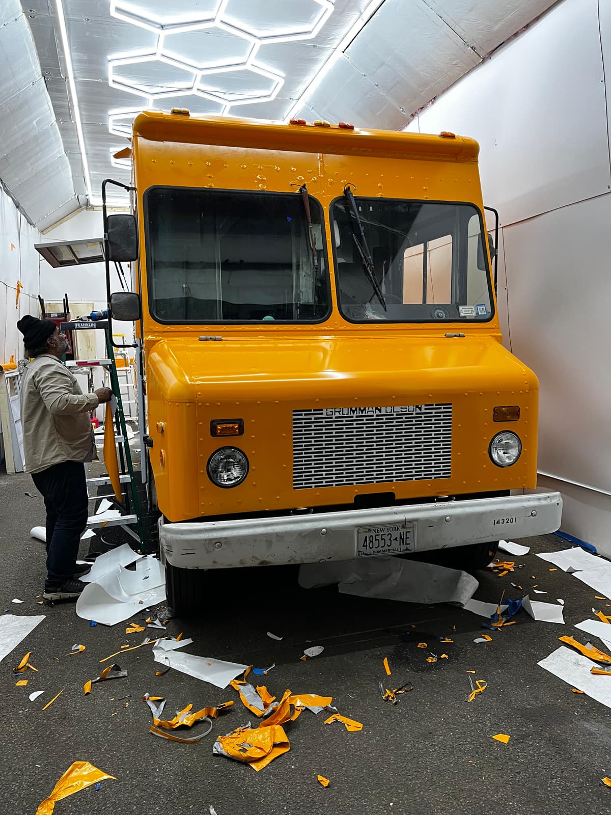Installer working at the front of an orange step van in the NYC Car Wraps shop