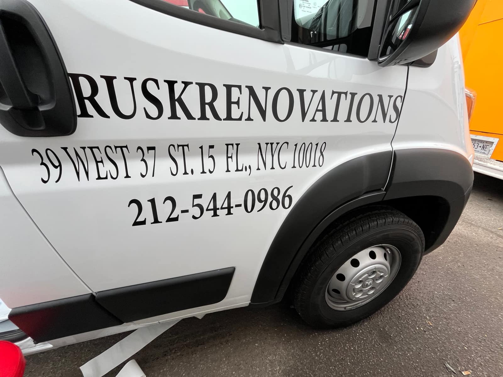 Side of a white van with large cut vinyl lettering reading Rusk Renovations, with the address and phone number below