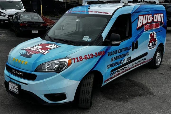 Light-blue Ram ProMaster City in a full printed wrap for Bug-Out Solutions, a Staten Island pest-control company, with lettering, phone number and 24-hour service badge, front three-quarter view in a lot