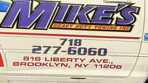 Close-up of Mike's Heavy Duty Towing lettering on a tow truck with a 718 phone number and a Liberty Ave, Brooklyn NY 11208 address