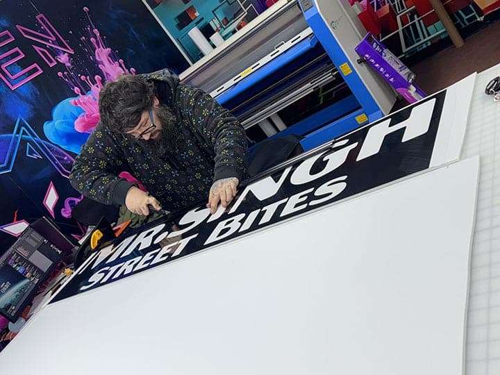 Installer trimming printed Mr. Singh Street Bites lettering on the table in the NYC Car Wraps shop