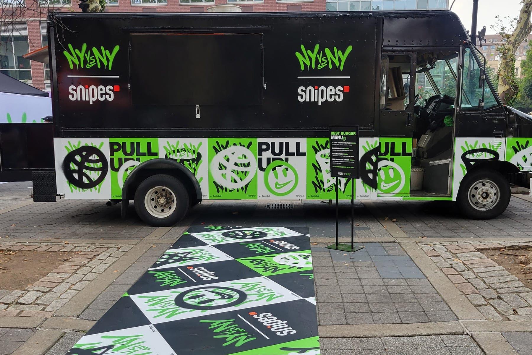 Black Snipes Pull Up campaign step van with green graphics parked at an event beside branded floor graphics and a checkered mat