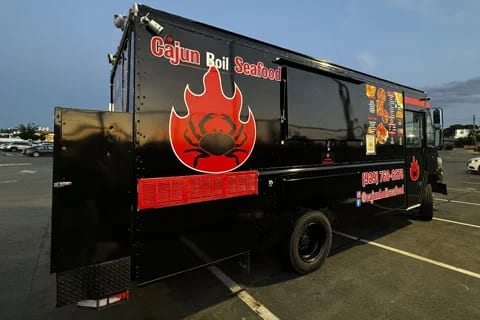 Black Cajun Boil Seafood truck with a red crab flame logo, side view at dusk